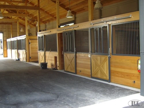 Row of horse stalls with mesh ventilation panels and natural wood construction in barn aisle