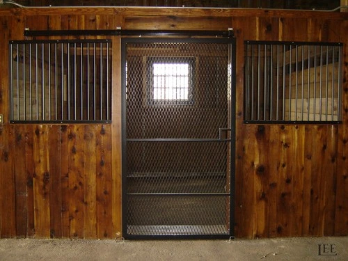 Natural wood stall front with wire mesh panel centered between vertical plank sections, brown floor visible