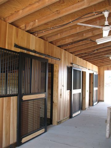 Natural wood sliding stall doors with black vertical bar upper grills and wire mesh panels in timber-frame barn