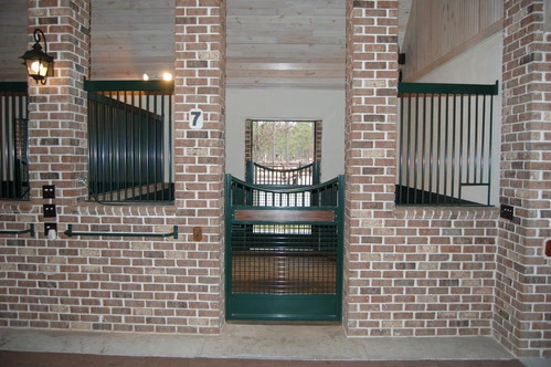 Dark green stall door centered in exposed brick wall with flanking windows