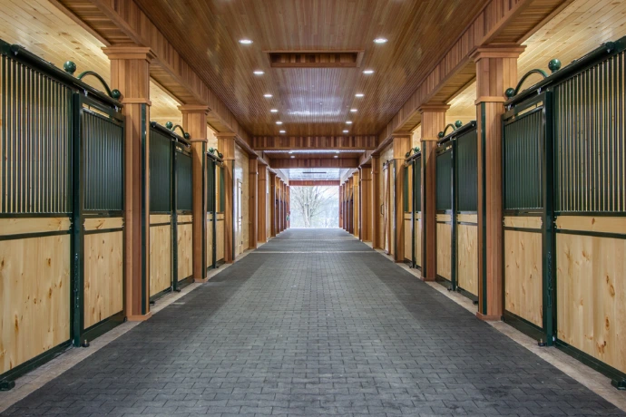 Long barn aisle with forest green stall fronts, natural pine lower panels and black vertical bar upper grills