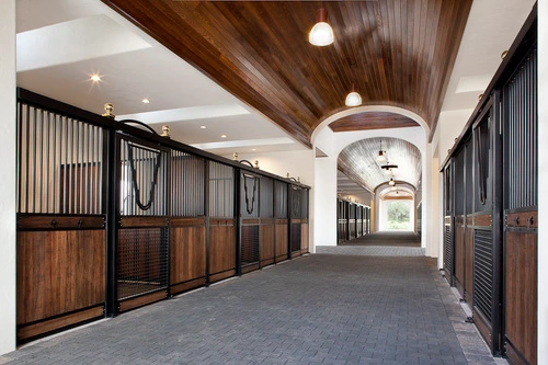 Barn aisle with black metal arched stall fronts, rich mahogany lower panels and circular pendant lights