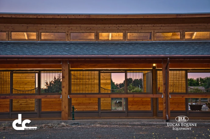 Two-level barn exterior showing natural wood stall fronts with multiple arched windows