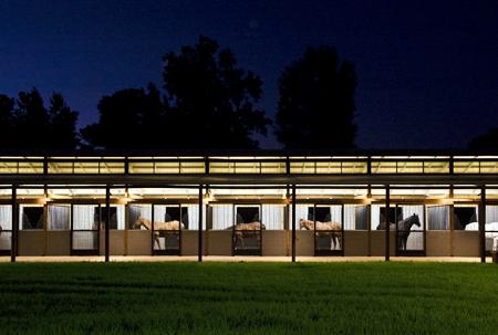 Night view of illuminated barn exterior with horizontal stall openings and outdoor lighting