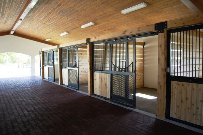 Covered barn aisle with black metal stall fronts, natural pine lower panels and decorative brick floor