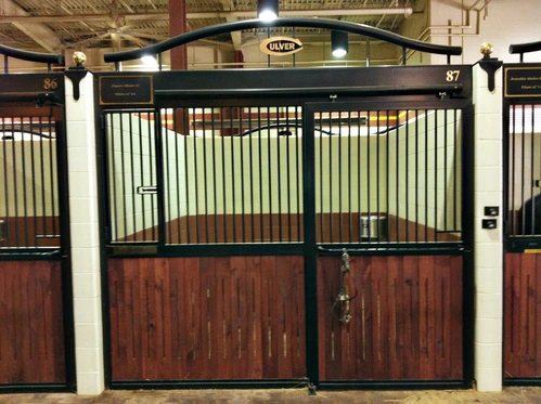 Mahogany stall front with black vertical bar upper grill overlooking outdoor pasture