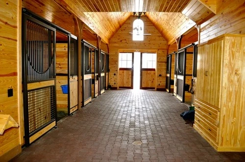 Brick floor barn aisle with mahogany stall fronts and wire mesh sliding doors