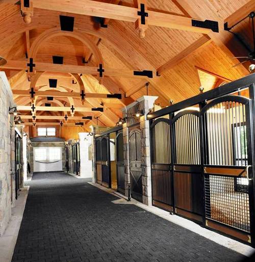 Elegant barn aisle with black metal arched stall fronts, mahogany lower panels and vaulted white ceiling