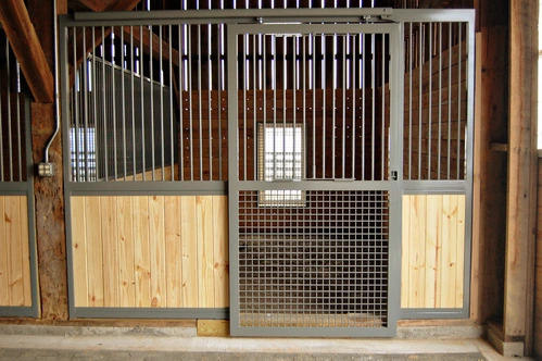 Natural pine stall fronts with black vertical bar upper grills and wire mesh lower panel in bright interior