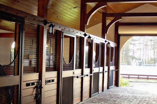Mahogany stall fronts with wire mesh upper panels and natural pine lower sections in covered outdoor barn