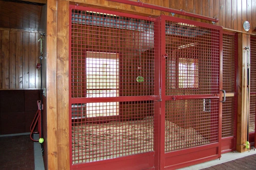 Red powder-coated wire mesh stall panel with window opening in dark wood paneled interior