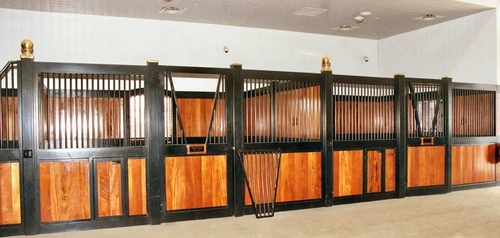 Black metal stall fronts with rich mahogany lower panels and horses visible in illuminated stalls