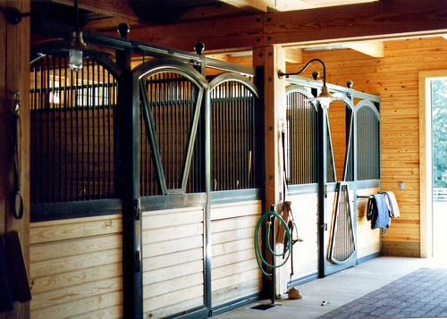 Black metal arched stall fronts with natural pine lower panels, wire mesh doors and handlers with horse