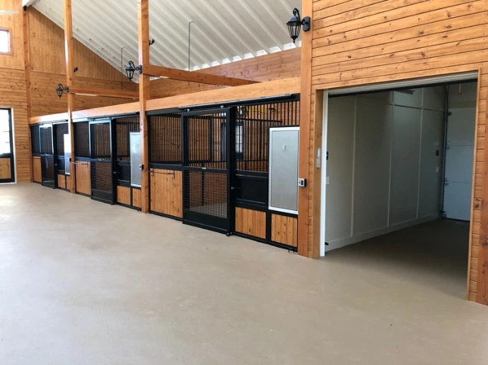 Modern barn aisle with black metal and natural wood stall fronts under timber-frame structure with corrugated metal roof