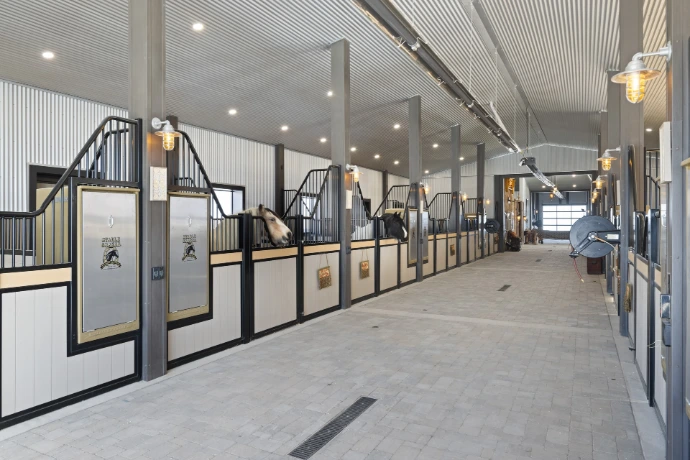 Long modern barn aisle with white stall fronts featuring black vertical bar upper grills along both sides