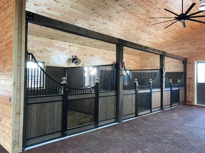 Black metal stall fronts with gray lower panels and wire mesh door sections in contemporary barn aisle