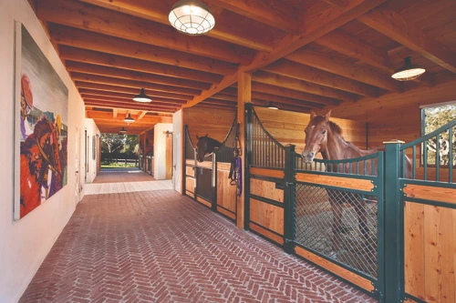 Teal painted stall fronts with natural pine lower sections and black vertical bars in brick floored barn aisle