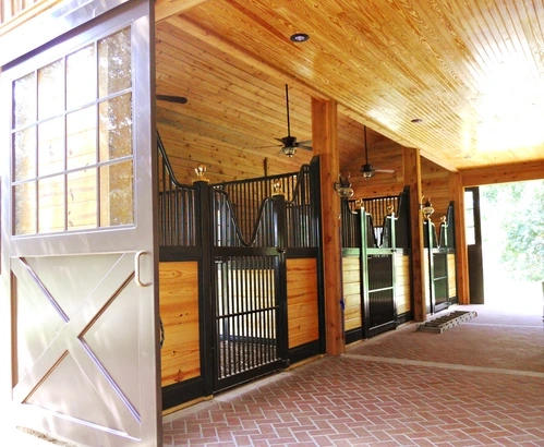 Dark wood stall fronts in timber-frame barn aisle with Dutch door entrance visible