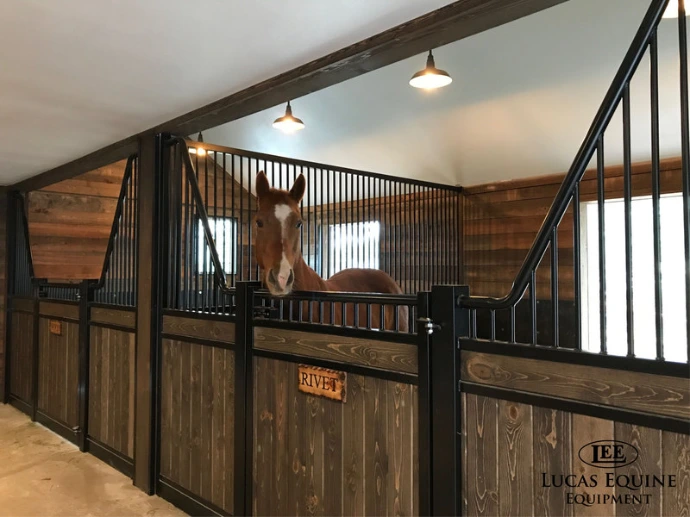 Dark wood stall fronts with black metal vertical bar upper grills in covered barn aisle with timber ceiling