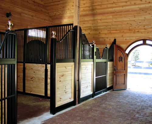 Forest green stall fronts with natural pine lower panels and black vertical bar upper grills in timber-frame barn