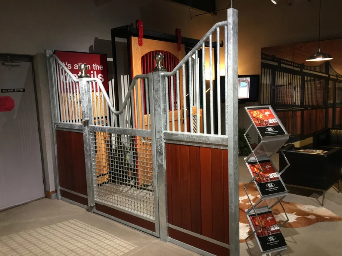 Mahogany stall fronts with wire mesh sliding doors and magazine rack mounted in white barn aisle