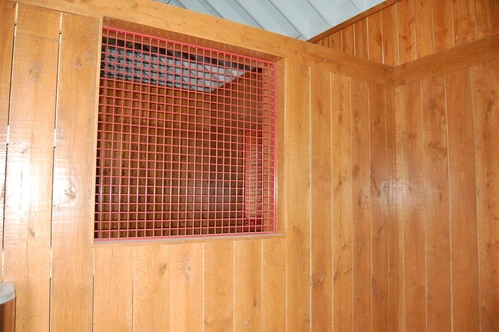 Natural pine stall wall with red mesh wire grill panel insert in wood ceiling barn