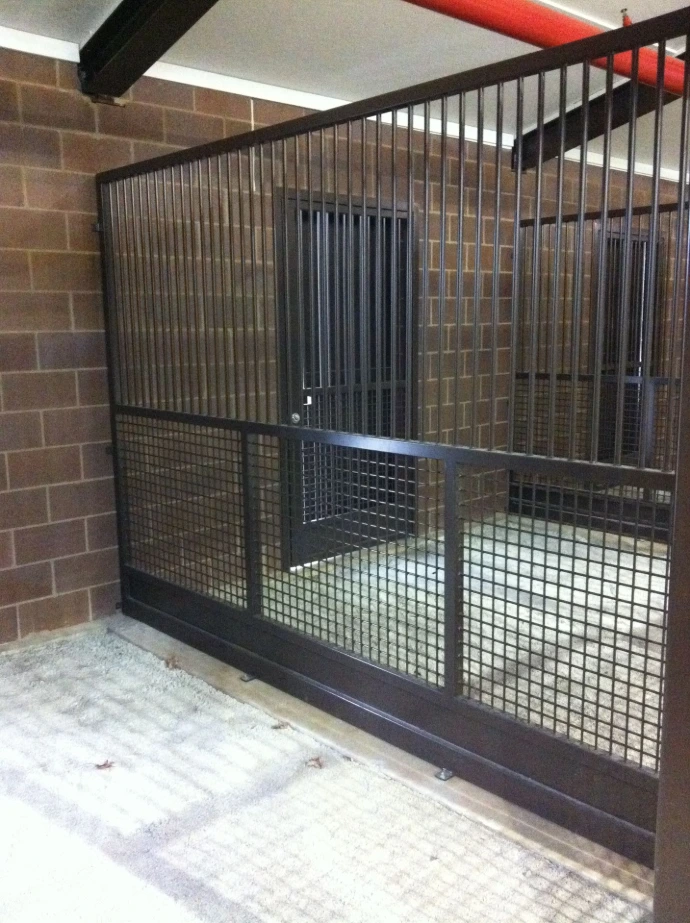 Black metal mesh grid stall partition in corner of brown brick building interior