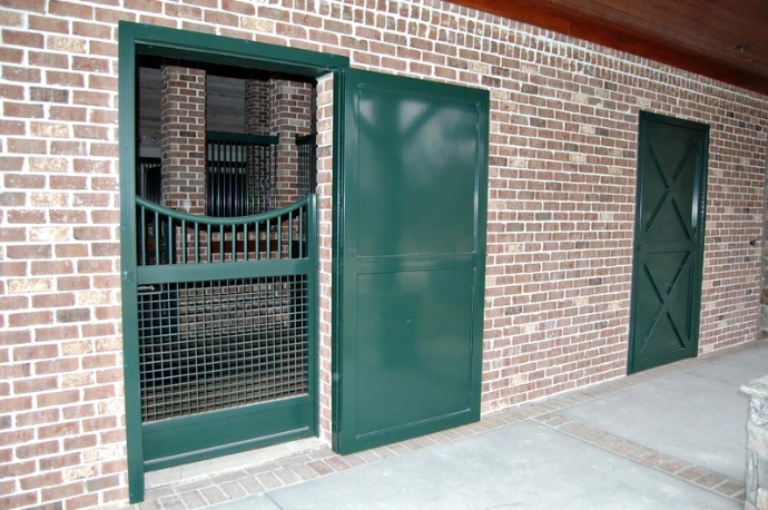 Teal stall door on red brick exterior with circular cutout in grid mesh panel and vertical bars