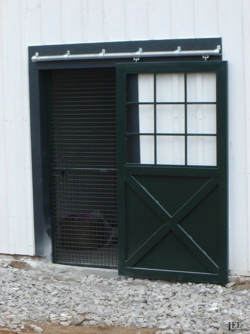 Dark green metal Dutch door with X-pattern lower panel and mesh upper section on white wall
