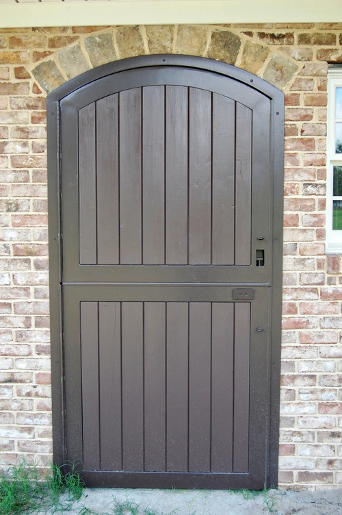 Gray vertical board Dutch door with metal hardware on red brick exterior wall