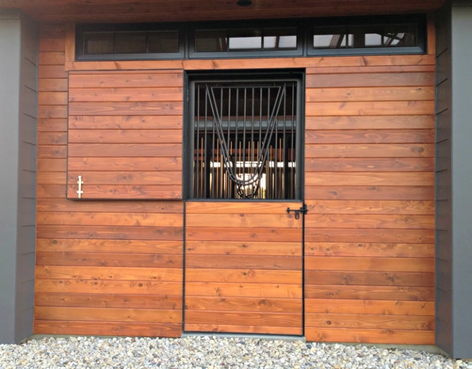 Rich mahogany sliding door with vertical black bar grill upper section on natural wood wall