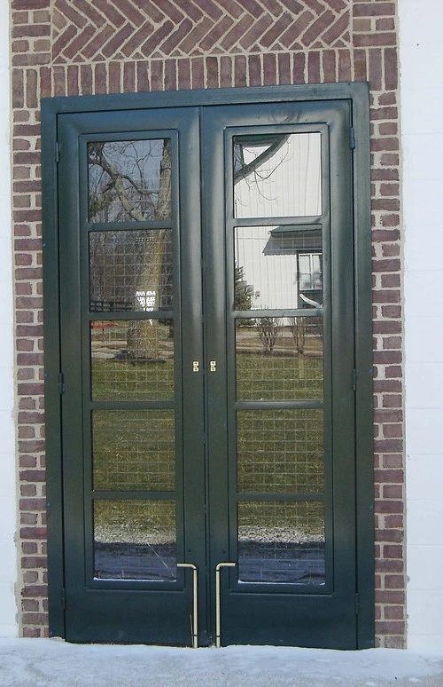 Dark green double doors with full-length glass panels on red brick building between columns