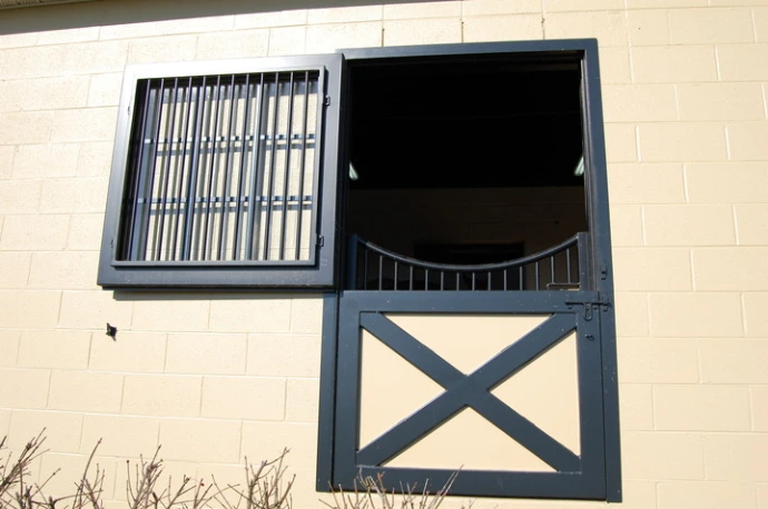 Black metal Dutch door with mesh upper panel and X-brace lower section on cream wall