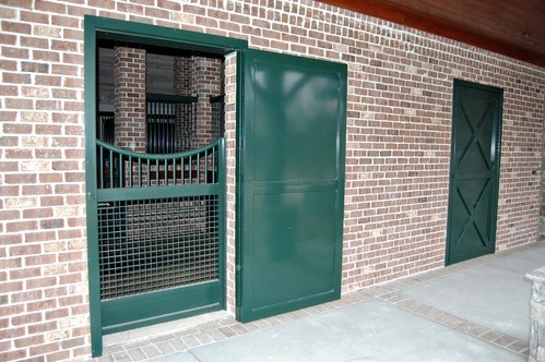Dark green sliding doors with wire mesh panels on red brick wall under covered area