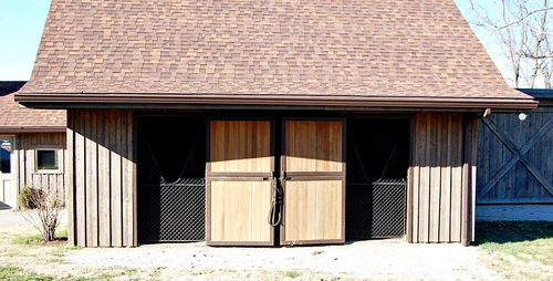 Barn with three dark sliding doors featuring mesh panels on tan horizontal siding under brown roof