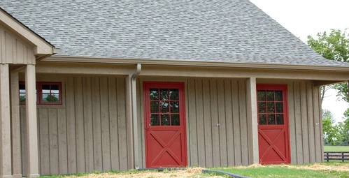 Beige barn with two burgundy doors featuring X-pattern and multi-pane window upper sections