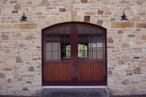 Dark mahogany arched double doors set in stacked stone archway wall