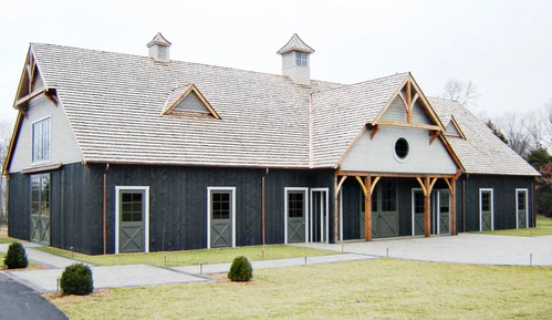 Modern barn complex with dark siding, white trim, timber-frame gable details and multiple dormers