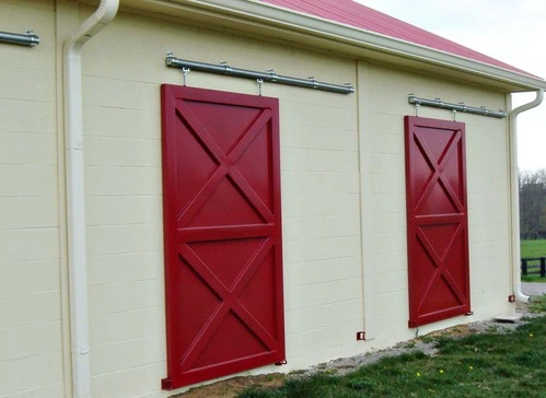 Cream colored barn with two burgundy X-pattern sliding doors under red metal roof