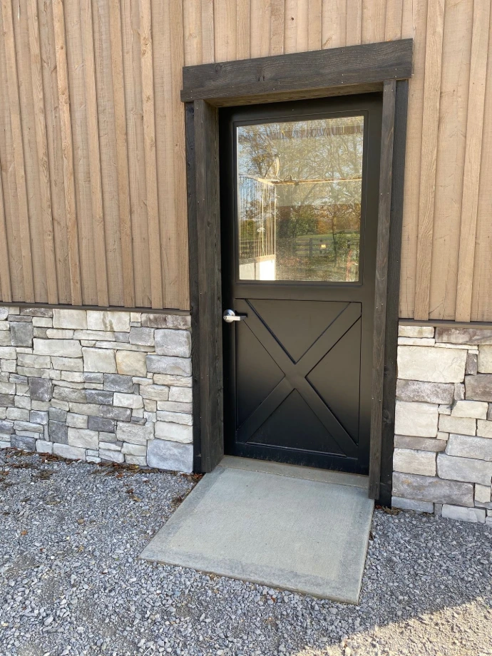 Black Dutch door with X-pattern lower panel on stacked stone and white stucco wall