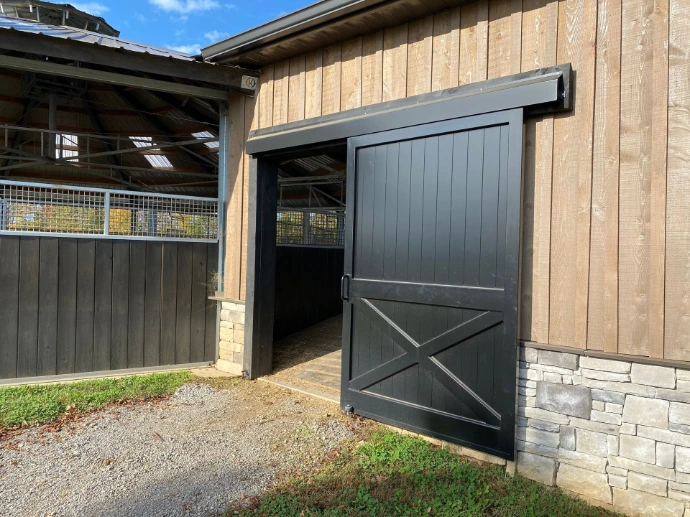 Black vertical plank sliding door partially open on natural pine board-and-batten barn wall