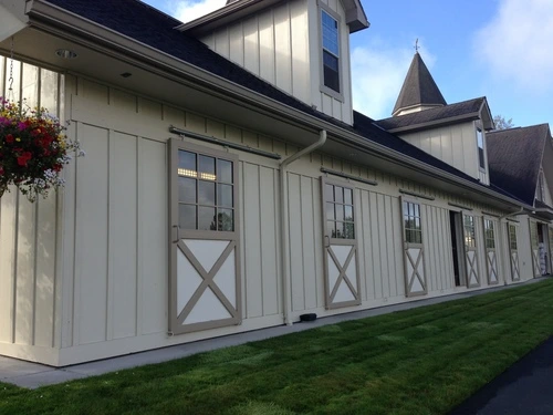 White painted barn with three natural wood X-pattern doors under black roof eaves