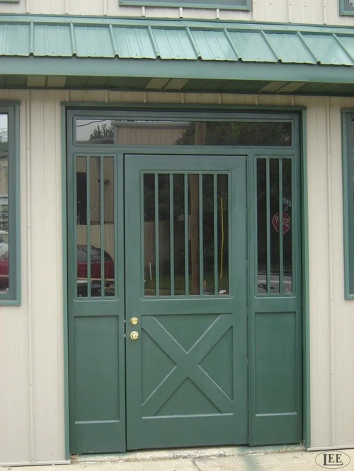 Sage green double doors with vertical bar upper grills and X-pattern lower panels on cream stucco