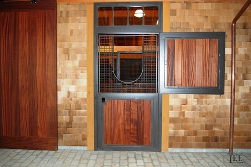 Interior barn view showing multiple stalls with varied wood tone Dutch doors and decorative metal grills