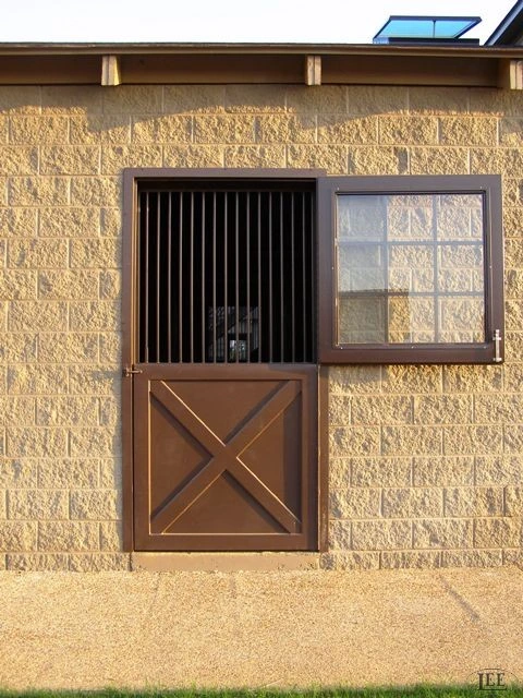 Natural wood Dutch door with black metal vertical bar grill upper section on textured limestone wall