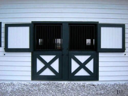 White horizontal siding barn with two black Dutch doors featuring X-pattern lower panels and frosted window sections