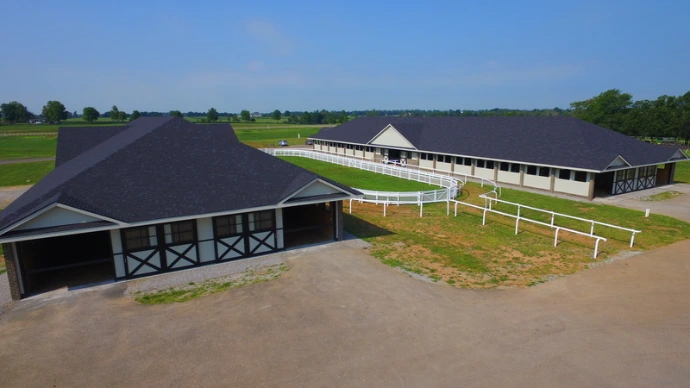 Long dark roofed barn complex with white board fencing in foreground