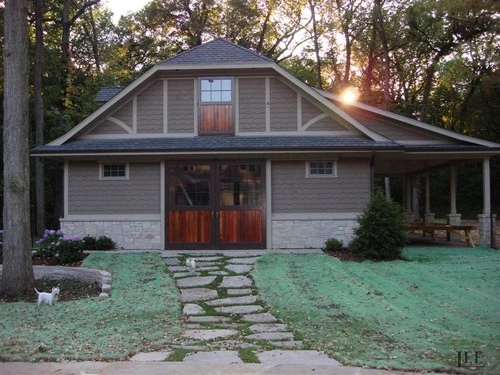Gray residential barn structure with arched wood door and stone walkway at dusk