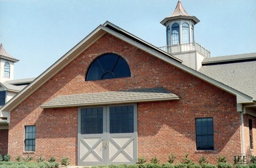 Red brick barn with white trim featuring arched gable and X-pattern stall doors