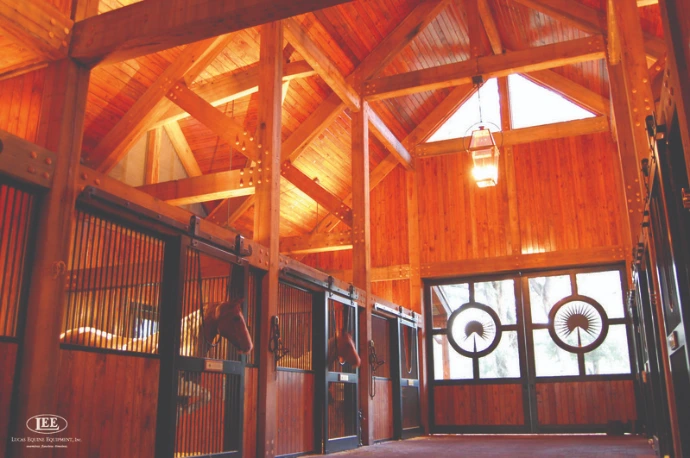 Timber-frame barn interior with natural wood stall doors and decorative metal grills